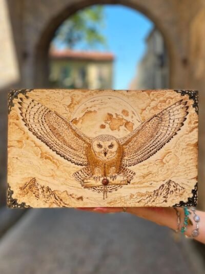 Gros plan sur la pyrogravure d’une chouette aux ailes ouvertes devant la lune sur une boîte à thé en bois